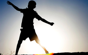 Silhouette profile of a young Indian boy dancing against hazy sun setting background showing lens flare. Image shot 2007. Exact date unknown.